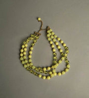 Yellow plastic necklace with three strands of beaded vintage jewelry with golden spacers.