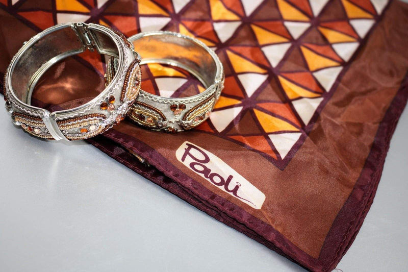 Set of 2 vintage hinged bangles with silver and golden metallic beading on a patterned cloth.